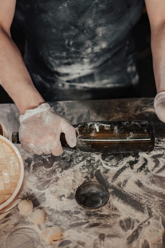 A close-up of a chef using a glass bottle to roll dough for dumplings.